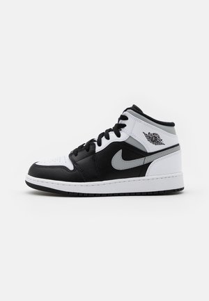 Czarno-biało-szary półwysoki sneaker Nike Air Jordan z czarnymi sznurowadłami i logo Air Jordan na kołnierzu wokół kostki, widok z boku.