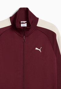 Mørkerød zip-up jakke med høj krave, cremefarvede detaljer på skuldrene, tekstureret stof og hvid Puma-logo på venstre bryst.