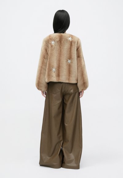 Kergelt tan värvi kunstkarusnahast jope, millel on hõbedased tähe kaunistused seljal, kombineeritud laia pruuni kunstnahkse pükste paariga. Sile tekstuur.