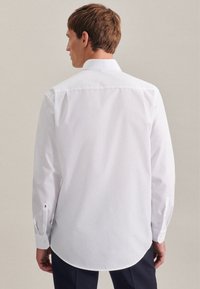 Chemise blanche à manches longues, avec col classique, texture lisse et ourlet arrondi. Comprend des poignets boutonnés avec accents.