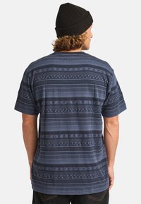Short-sleeve shirt in dark blue, featuring horizontal striped patterns with varying textures and geometric accents. Soft fabric, relaxed fit.
