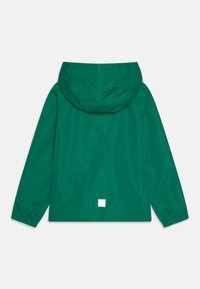 Grön vattentät jacka med huva, elastiska ärmslut och en fyrkantig logotyp på den nedre delen av ryggen. Slät yta, minimalistisk design.