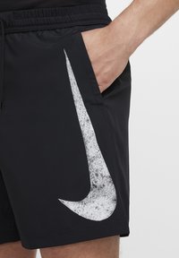 Fekete sportos rövidnadrág sima anyagból, a bal oldalon egy feltűnő textúrájú fehér Nike pipa logóval. Rugalmas derékpánt zsinórral.