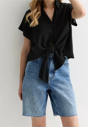 Black short-sleeve button-up shirt with a front knot paired with high-waisted blue denim shorts featuring a frayed hem.