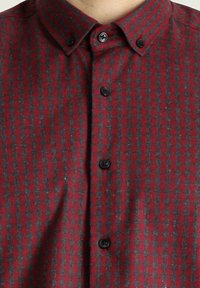 Camisa de cuadros roja y gris de botones, fabricada con una tela suave, que cuenta con botones negros y un diseño de cuello tradicional.