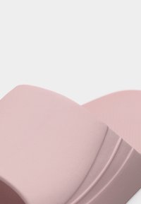 Pehmeän vaaleanpunaiset vaahtomuoviset korokepohjasandaalit leveillä remmeillä ja kuvioidulla pohjalla, lähikuvassa valkoisella taustalla.