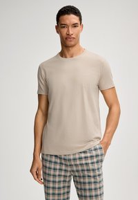 Beige kortærmet t-shirt lavet af blødt stof med et diskret logo på venstre bryst, parret med plyssede pyjamabukser i lyse nuancer.