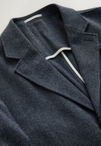 Dunkelblazer aus Fischgrat mit Reverskragen, aus strukturiertem Stoff und mit einem kontrastierenden cremefarbenen Futter im Inneren.