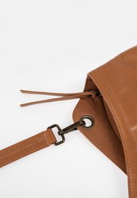 Braune Ledertasche mit glatter Oberfläche, ausgestattet mit einem abnehmbaren Tragegurt und einem Metallverschluss. Das offene Design zeigt den Innenraum.