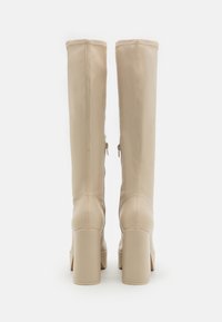Botas beiges hasta la rodilla en material sintético suave, con corte recto, cremalleras en la parte trasera y tacones gruesos.
