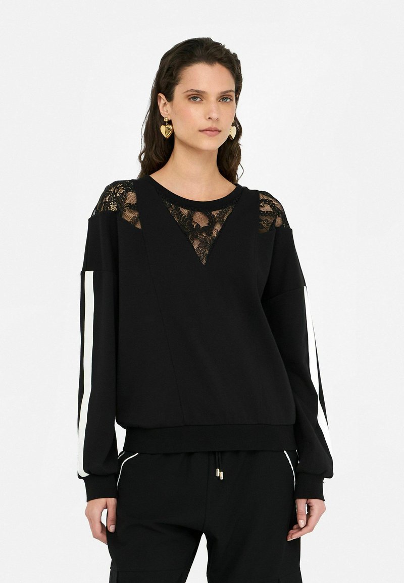 Sweatshirt noir avec un design de panneau en dentelle aux épaules et au col. Manches longues avec des rayures blanches sur les côtés, coupe décontractée.