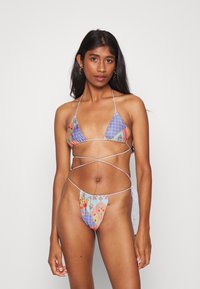 Biquíni triangular em tecido estampado com padrões em azul, roxo e flores. Apresenta atilhos finos e cobertura mínima em um estilo de dois peças.
