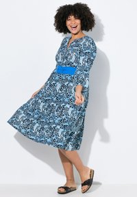 Kleid mit Jaguar-Print in Blau und Schwarz, knielang, mit V-Ausschnitt und Dreiviertelärmeln. Besitzt einen breiten blauen Gürtel in der Taille.