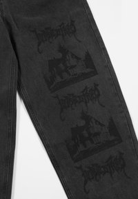 Pantaloni in denim neri con una grafica distressed ripetuta di una casa e testo stilizzato, con una finitura opaca e dettagli audaci a contrasto.