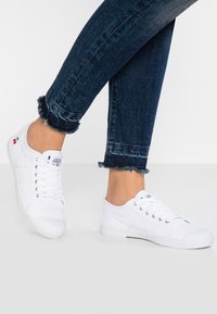 Baskets en toile blanches avec un design à lacets et une semelle en caoutchouc. Présente un détail cerise brodé. Portées avec un jean en denim foncé, à l'ourlet effiloché.