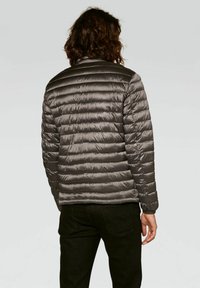Gray, puffer jacket with horizontal stitching, ribbed collar, lightweight texture, and elastic cuffs, viewed from the back. Black pants visible.