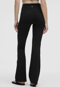Schwarze Leggings mit einem enganliegenden hohen Bund, ausgestelltem Saum und Logodetail. Hergestellt aus glattem, dehnbarem Material für optimalen Komfort.