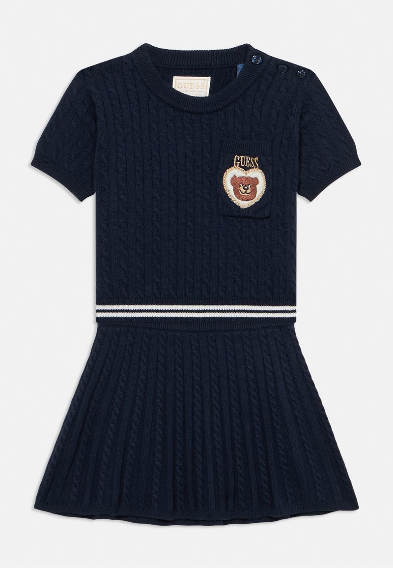 Marineblå kabelstrikket kjole med korte ærmer, med en lille lomme og et broderet bjørnemotiv. Vandret hvidstribet taljebånd.