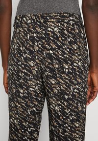 Zwarte broek met patroon, voorzien van een gestructureerd oppervlak met abstracte ontwerpen in crèmekleurige en bruine tinten, met een getailleerde pasvorm en een middelhoge tailleband.