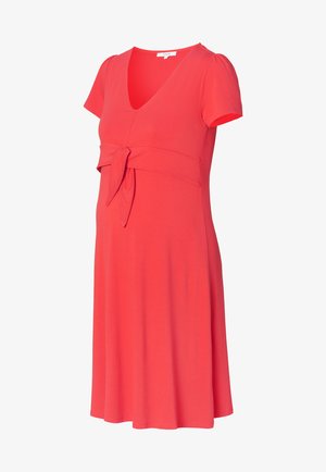 Schwangerschafts Kleid in Korallenfarbe, aus weichem Stoff. Mit V-Ausschnitt, kurzen Ärmeln und einem vorderen Bindedetail unter der Brust für einen figurbetonten Look.