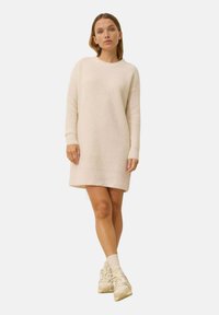 Szydełkowana kremowa sukienka z długimi rękawami i żeberkowym wykończeniem; ma teksturowany wzór. Noszona z kremowymi skarpetkami i masywnymi beżowymi sneakersami.