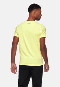 Gul kortærmet t-shirt med rund halsudskæring, der har et lille logo på den øverste del af ryggen. Materialet ser blødt og let ud.