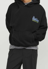 Felpa nera in misto cotone, con tasca frontale, cappuccio regolabile con cordino e design ricamato sul petto in blu e verde.