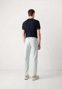 Pantaloni din bumbac de culoare albastru deschis, cu o croială ajustată, asociați cu un polo de culoare bleu închis, cu margini albe. Vedere din spate, fundal neutru.