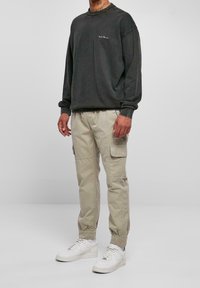 Sudadera de tela gris oscuro con cuello redondo y logo. Pantalones cargo beige con bolsillos laterales, combinados con zapatillas blancas.