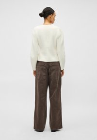 Krēmkrāsas džemperis ar garām piedurknēm, apaļu izgriezumu un piegulošu apakšu, kopā ar vaļīgām brūnām samta biksēm ar divām aizmugurējām kabatām.