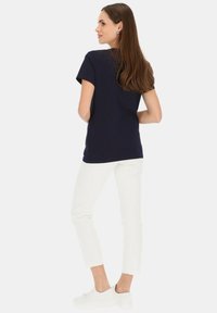 Granatowa bluzka z krótkim rękawem o luźnym kroju. Połączona z białymi spodniami cropped i białymi trampkami, charakteryzującymi się gładką fakturą materiału.