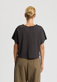 Maglietta grigia scura a maniche corte, con una vestibilità ampia e una sottile texture a righe. Presenta un colletto rotondo e dettagli sulla cucitura posteriore. Abbina pantaloni marrone chiaro.