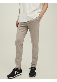 Pantalon beige coupe slim avec poches latérales, en tissu doux, associé à des baskets noires avec des accents blancs. Design de jambe légèrement fuselé.