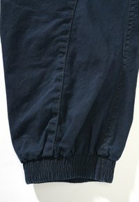 Pantalones elásticos de un oscuro color navy con puños fruncidos, que presentan una textura lisa y ligeramente arrugada, además de costuras laterales.