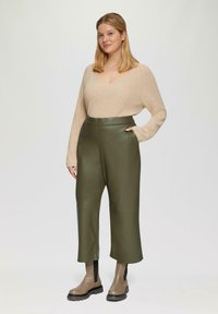 Beige geribbelde trui met een V-hals, gecombineerd met hoog-wijde groene leren broeken en taupe enkellaarsjes met zwarte zolen.