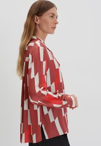 Rood en wit gemusterd shirt met een losse pasvorm, lange mouwen en een knoopsluiting, met een lichte split aan de onderrand.