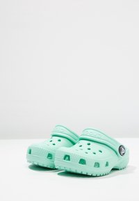 Lichtblauwe Crocs klompen met een gevormd ontwerp, ventilatiegaten en een achterkantband. De textuur is glad met een geribbelde zool voor grip.