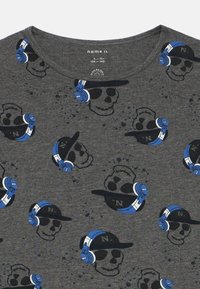 Temno siva majica z ponovljenimi lobanjami, ki nosijo črne kape z oznako "N." in modre slušalke, natisnjene po tkanini.