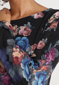 Schwarze Bluse mit floralem Muster, die große, mehrfarbige Rosenmuster zeigt, mit lockerem Schnitt und plissierten Details an den Ärmeln. Aus glattem, leichtem Stoff.