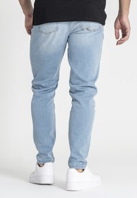 Jeans ajustados de color azul claro con una textura suave, que cuentan con bolsillos traseros cosidos y un dobladillo limpio, combinados con zapatillas blancas.