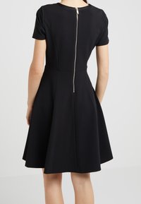 Černé krátké šaty s upnutým korzetem, rozšířenou sukní a kovovým zipem na zadní straně. Hladká látka s mírným leskem.