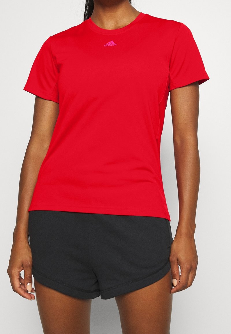 Camiseta deportiva roja hecha de material transpirable, con un escote redondo y mangas cortas, adornada con un pequeño logo rosa en el pecho.