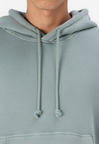 Lys grøn hoodie med snørebånd med knyttede ender, en blød tekstur og en kængurulomme foran.