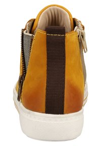 Zapatilla amarilla y marrón con un exterior de piel suave, panel lateral texturizado y cremallera trasera. Suela de goma blanca y detalles de costura.