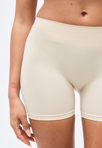 Shorts beige sans coutures fabriqués en matière légère et extensible. Ils présentent une finition lisse et une ceinture confortable pour faciliter les mouvements.