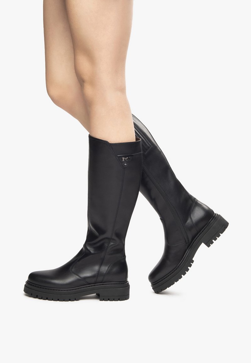 Black knee-high boots made of smooth leather. Chunky rubber sole with textured tread. Features a side zip and decorative hardware accents.