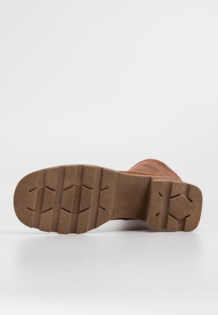 Bota de ante marrón con suela de goma texturizada, que presenta un patrón hexagonal para tracción y durabilidad. Líneas limpias y diseño de puntera redondeada.