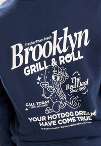 Sudadera azul marino con texto blanco que dice "Brooklyn Grill & Roll," con un gráfico de un perrito caliente de dibujos animados y detalles de contacto.