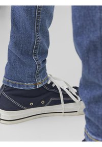 Mörkblå canvas sneakers med vita snören, gummisulor och kontrasterande sömmar, kombinerat med ljusblå, åtsittande denimjeans med gula trådar.