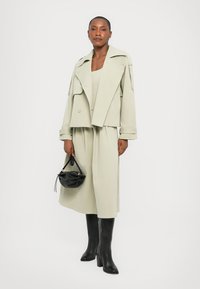 Light green double-breasted jacket, matching dress, and knee-high black boots. Small black handbag with a curved shape and top handle.